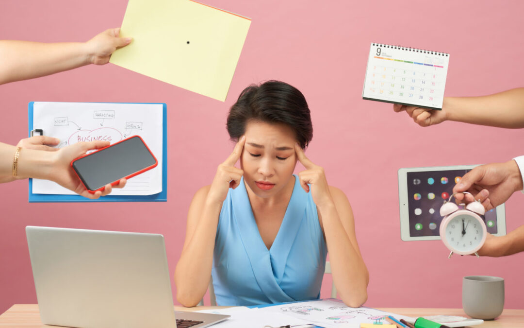 Overworked young employee refuses all things, frowns face in annoyance, sits at desktop with paper documents and notepad, isolated over pink background. Female workes bothered by many questions